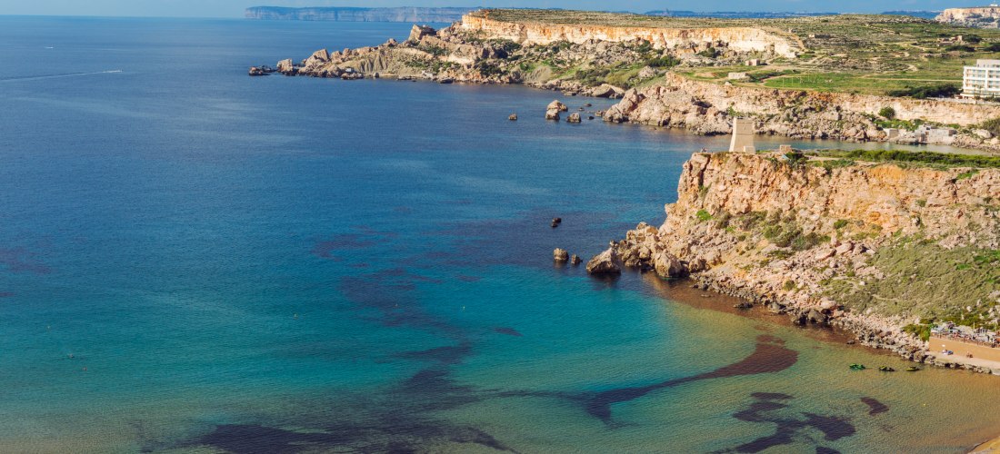 Ghajn Tuffieha Bay auf Malta mit goldfarbenem Sandstrand, türkisblauem Meer und steilen Felsklippen