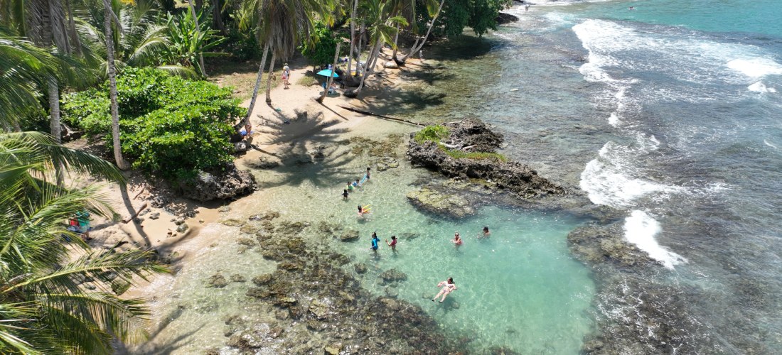 Menschen baden in einem natürlichen Pool zwischen Felsen an einem tropischen Strand mit Palmen und türkisblauem Meer