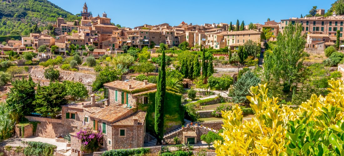 Malerisches Dorf im Tramuntana-Gebirge auf Mallorca mit traditionellen Steinhäusern, Gärten und Bergen im Hintergrund