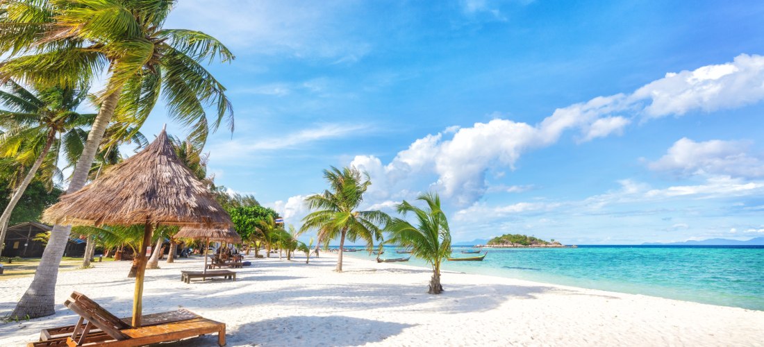 Idyllischer tropischer Strand mit Palmen, Strohhütten und türkisblauem Meer