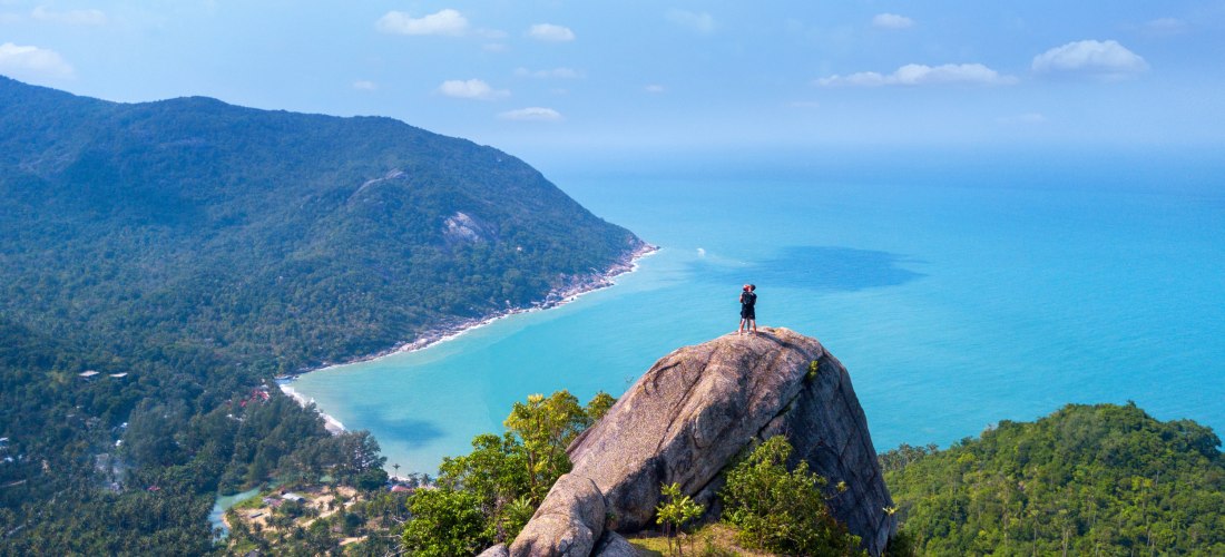 Person steht auf einem hohen Felsen mit weitem Blick über Meer und bewaldete Küste. ( Koh Phangan Island )