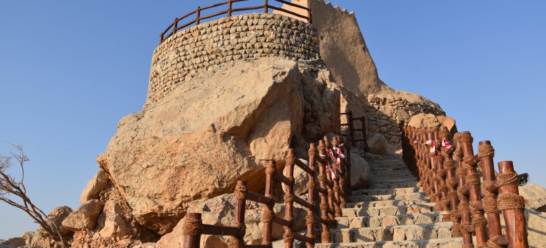 Steintreppe mit Holzgeländern führt zum Dhaya Fort in Ras Al Khaimah – historisches Wahrzeichen auf einem Hügel.