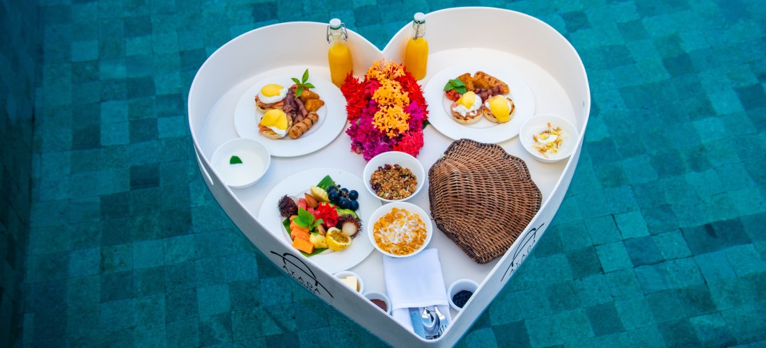 Ein romantisches Frühstück auf einem schwimmenden Tablett in Herzform, serviert im Pool. Frische Früchte, Eier, Säfte und Müsli sorgen für einen perfekten Start in den Tag in luxuriösem Ambiente.