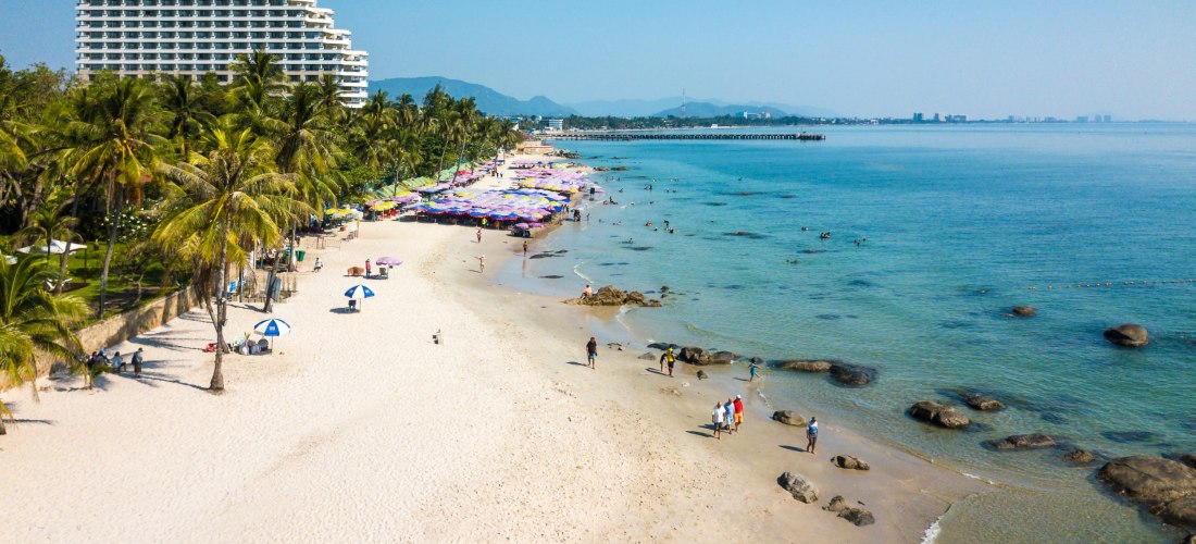 Strand von Hua Hin mit Palmen und Hotelresort Breiter Sandstrand mit Palmen und Hotel am Meer in Hua Hin, Thailand – beliebtes Reiseziel für Badeurlaub