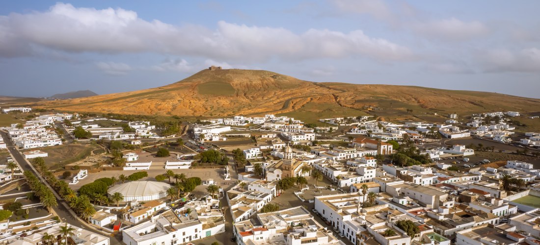 Luftaufnahme von Teguise auf Lanzarote mit weißen Häusern und dem Castillo de Santa Bárbara auf einem Hügel im Hintergrund.