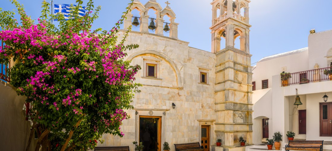 Innenhof des Klosters Panagia Tourliani in Ano Mera auf Mykonos mit Glockenturm, Steinbänken und blühender Bougainvillea