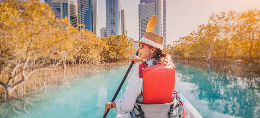 Frau paddelt im Kajak durch die Mangroven von Abu Dhabi mit Blick auf die Skyline