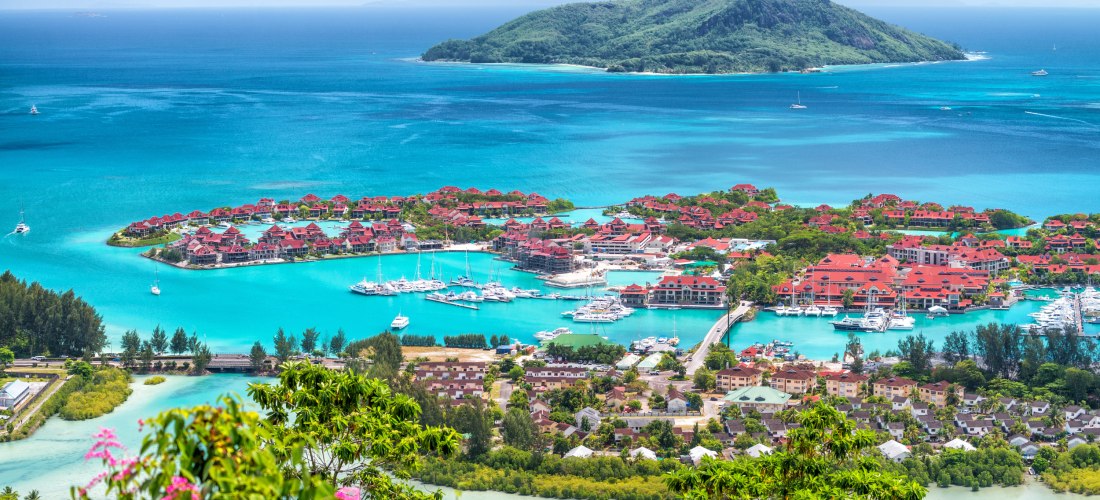 Luftaufnahme der Insel Mahé. Türkisblaues Wasser, luxuriöse Villen und einem eleganter Yachthafen. Die üppige Vegetation und die roten Dächer verleihen der Szene eine idyllische Atmosphäre.