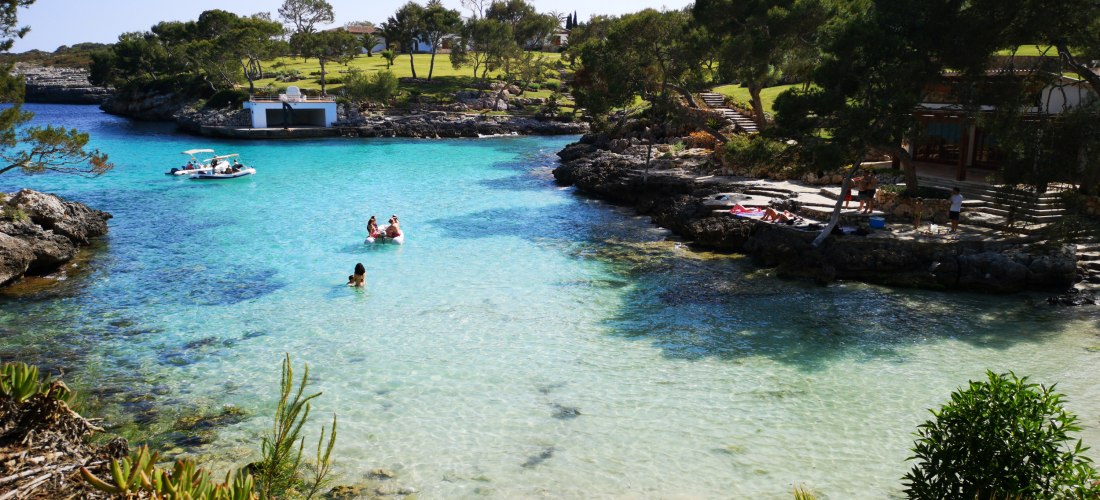 Ruhige Bucht mit türkisfarbenem Wasser, Badegästen und üppiger Vegetation in Cala Serena auf Mallorca