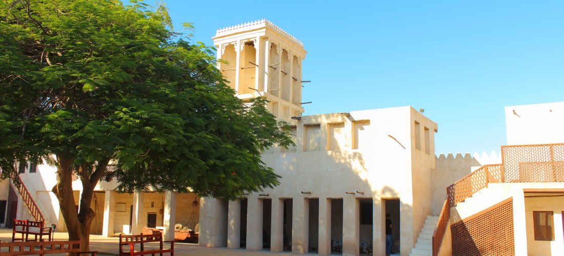 Innenhof des Nationalmuseums Ras Al Khaimah mit traditioneller Architektur, Windturm und schattenspendendem Baum.