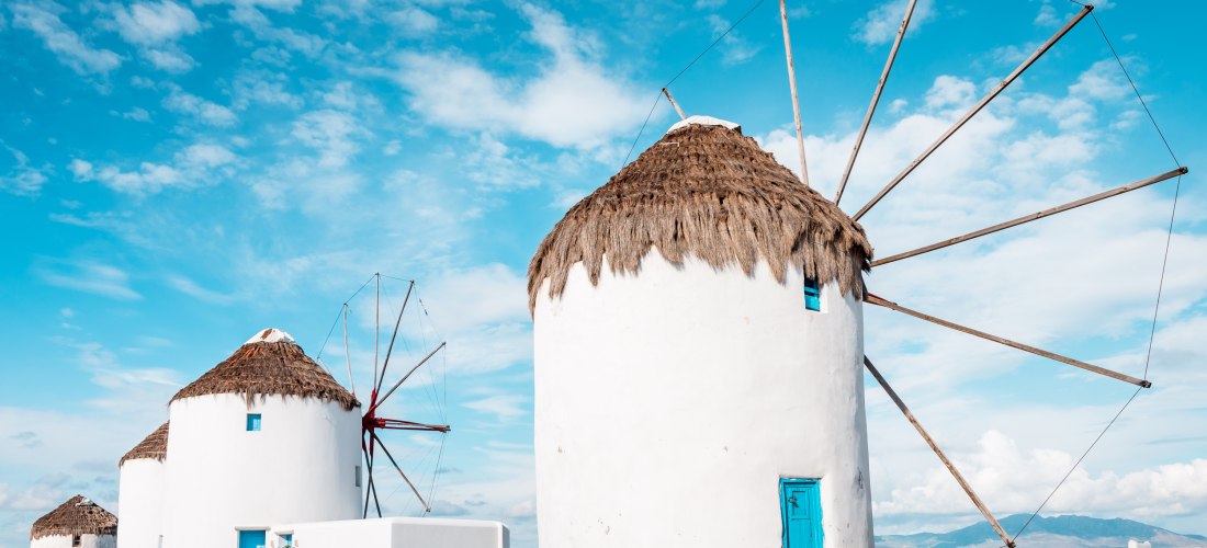 Traditionelle Windmühlen von Mykonos mit weißen Rundbauten und Strohdächern vor blauem Himmel