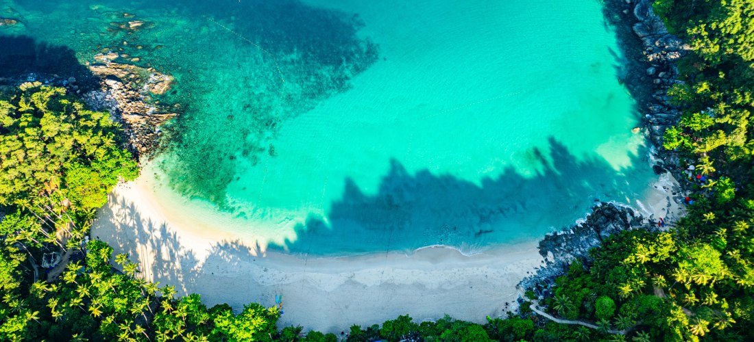 Luftaufnahme des Freedom Beach auf Phuket mit kristallklarem Wasser, weißem Sandstrand und umgebendem tropischen Regenwald.