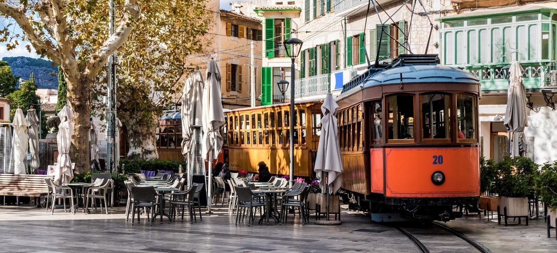 Historische Straßenbahn in Sóller auf Mallorca, die durch den Ortskern mit Cafés und Plätzen fährt
