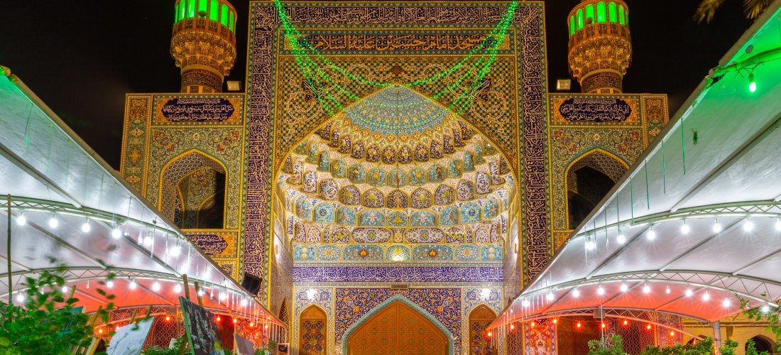 Der Eingang zur Imam-Hussein-Moschee in Dubai mit bunten Kacheln, einer Fassade im persischen Stil und einer Beleuchtung in den Farben der Nationalflagge der Vereinigten Arabischen Emirate, Kunstausstellung
