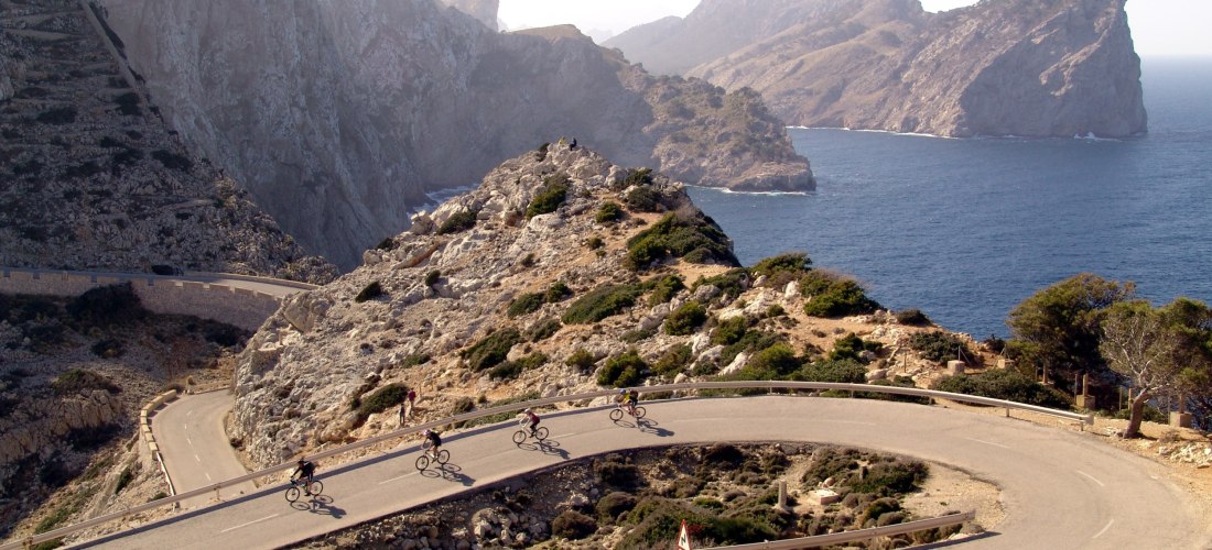 Radfahrer auf kurvenreicher Küstenstraße am Cap de Formentor auf Mallorca mit Blick auf das Meer und steile Felsen