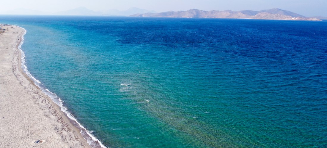 Weitläufiger Sandstrand auf Kos mit türkisblauem Meer und Inseln am Horizont