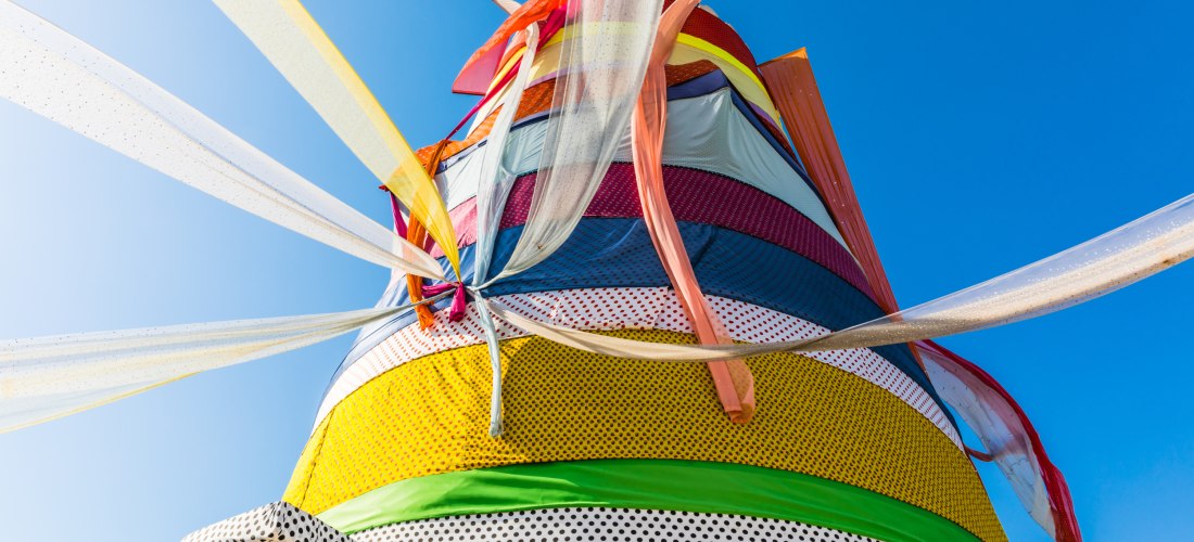 Farbenfrohe Kunstinstallation mit bunten Stoffbahnen, die im Wind flattern, vor klarem blauem Himmel