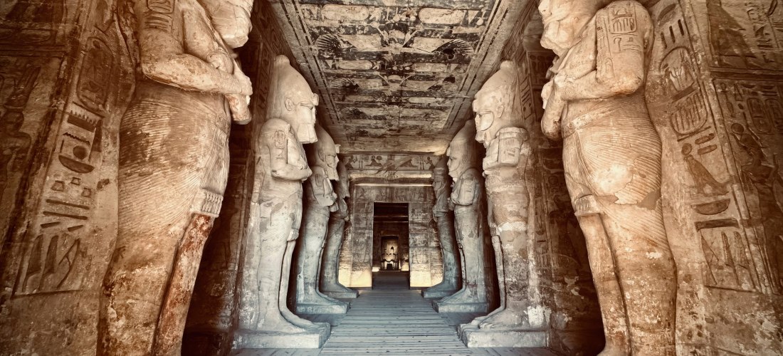 Das Bild zeigt den beeindruckenden Säulengang im Inneren des Tempels von Abu Simbel. Beidseitig des Ganges stehen monumentale Statuen des Pharaos Ramses II. in der Gestalt des Gottes Osiris. Die Wände und Decken sind mit gut erhaltenen Hieroglyphen und Re