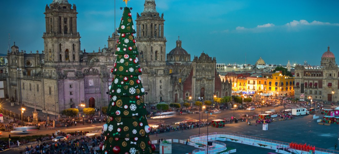Großer Weihnachtsbaum mit Lichtern und Ornamenten auf dem Zócalo-Platz in Mexiko-Stadt, mit der Kathedrale und beleuchteten Gebäuden im Hintergrund