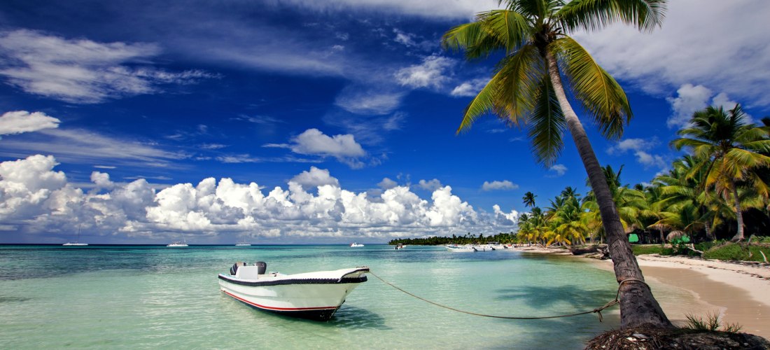 Weißer Sandstrand mit türkisblauem Meer, Palmen und Boot an der Küste von Isla Saona, Dominikanische Republik