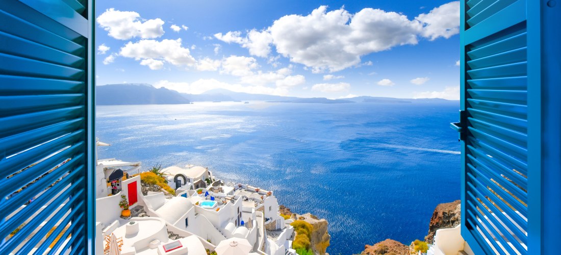 Blick durch ein offenes Fenster mit blauen Fensterläden auf die Caldera, das Meer und das weiße Dorf Oia auf der Insel Santorin, Griechenland