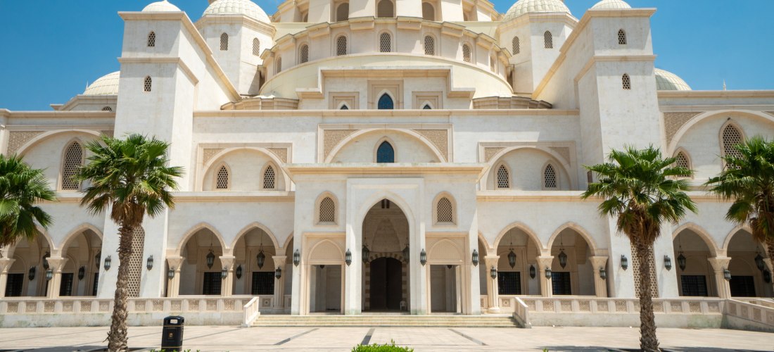 Frontansicht der Scheich-Zayid-Moschee in Fujairah, Vereinigte Arabische Emirate. Prunkvolle weiße Kuppeln, Palmen und Springbrunnen – eindrucksvolle Sehenswürdigkeit.