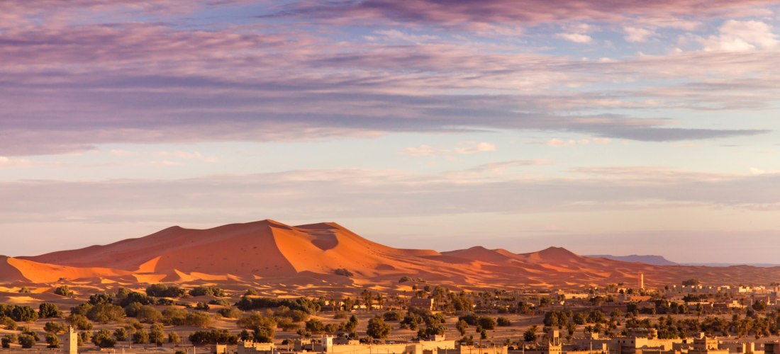 Blick auf das Wüstendorf Merzouga mit den beeindruckenden Sanddünen des Erg Chebbi im Hintergrund – beliebtes Reiseziel in der Sahara Marokkos.