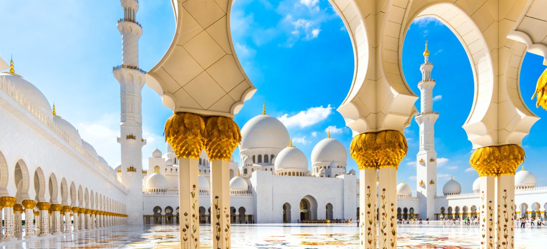 Blick durch verzierte Bögen auf die Sheikh Zayed Moschee in Abu Dhabi mit weißen Kuppeln und Minaretten