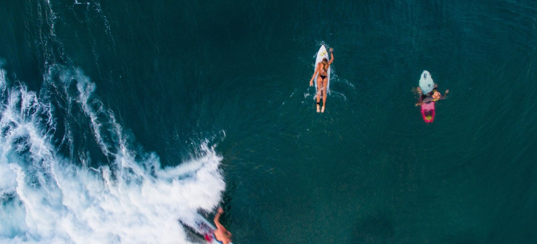 Surfer im türkisblauen Meer von Bali, während andere Surfer auf ihren Boards auf die nächste Welle warten