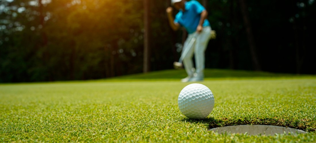 Golfball kurz vor dem Einlochen, mit Golfer im Hintergrund, der seinen Schlag beobachtet