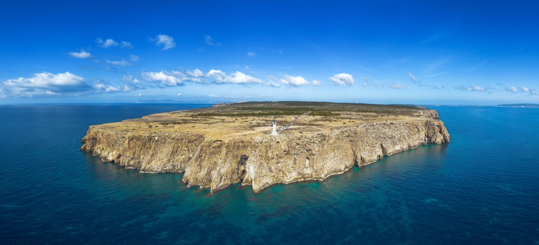 Steilklippen am Cap de Barbaria auf Formentera mit dem weißen Leuchtturm in der Mitte. Weite, karge Landschaft über dem türkisblauen Mittelmeer.