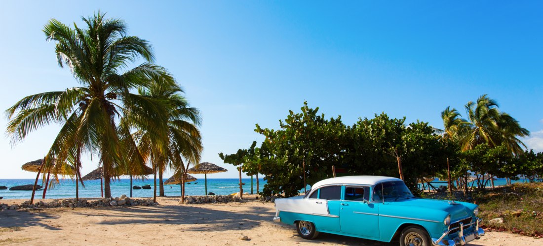 Klassischer Oldtimer in Blau-Weiß unter Palmen an einem karibischen Strand