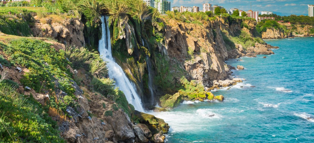 Die Unteren Düden-Wasserfälle in Antalya stürzen von den Klippen direkt ins Mittelmeer, umgeben von grüner Vegetation und Stadtgebäuden