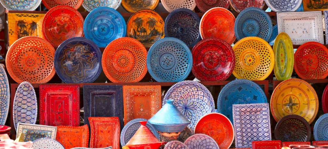 Farbenfrohe, handgefertigte Keramikteller und -schalen auf einem Marktstand. Die Teller sind in lebendigen Farben wie Rot, Blau, Gelb und Orange bemalt, mit detailreichen Mustern und traditionellen Designs. Ein wahres Fest für die Sinne.