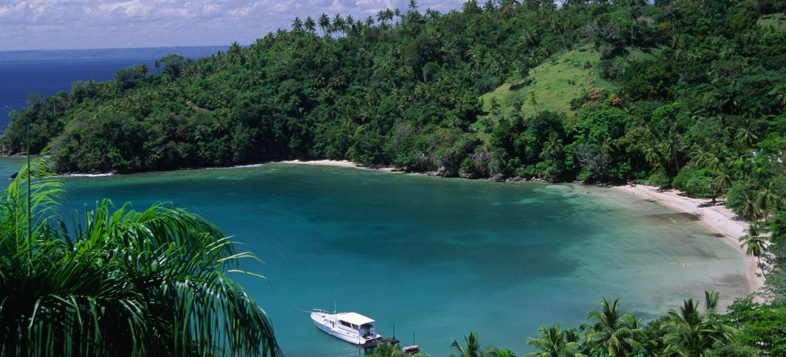 Idyllische Bucht bei Samaná in der Dominikanischen Republik mit türkisblauem Wasser, üppig grünen Hügeln und einem Boot am Ufer
