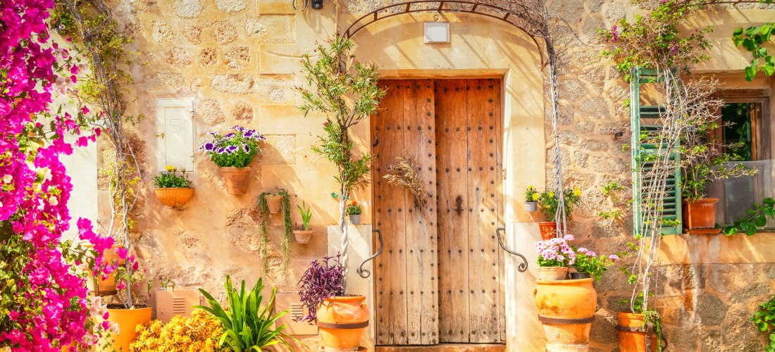 Rustikale Holztür eines traditionellen mallorquinischen Hauses, umgeben von Blumentöpfen und mediterraner Dekoration