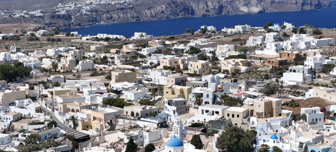 Panorama von Megalochori, Santorini: weiße Kykladenhäuser und Kuppelkirchen, dahinter die Caldera-Klippen und das tiefblaue Meer