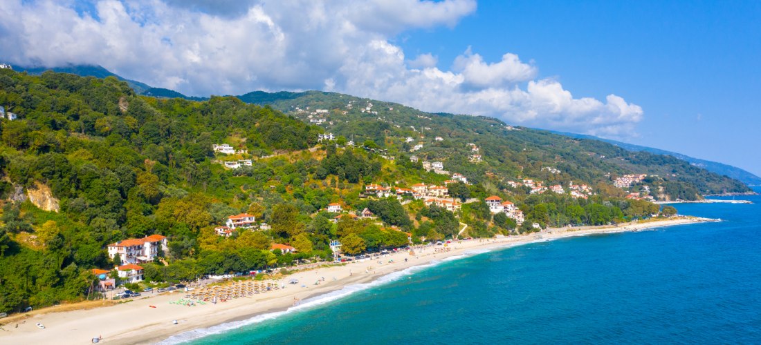 Luftaufnahme des Strandes von Agios Ioannis Damouchari auf der Pilion-Halbinsel in Griechenland mit türkisblauem Meer und grünen Hügeln im Hintergrund.