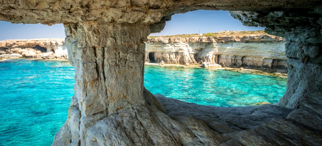 Blick aus einer Meeresgrotte bei Kap Greco auf Zypern auf türkisblaues Wasser und helle Kalkklippen der Sea Caves.