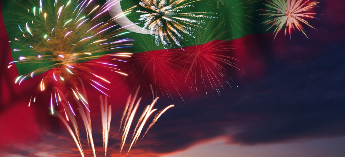 Ein spektakuläres Feuerwerk erleuchtet den Himmel vor der Nationalflagge der Malediven. Die bunten Lichter spiegeln sich in der Abenddämmerung und schaffen eine feierliche Atmosphäre.