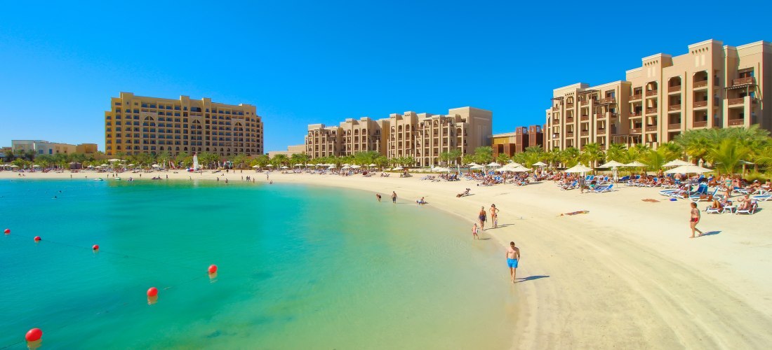 Luxuriöser Hotelstrand mit türkisblauem Wasser, Sonnenliegen und Menschen, die am Ufer spazieren