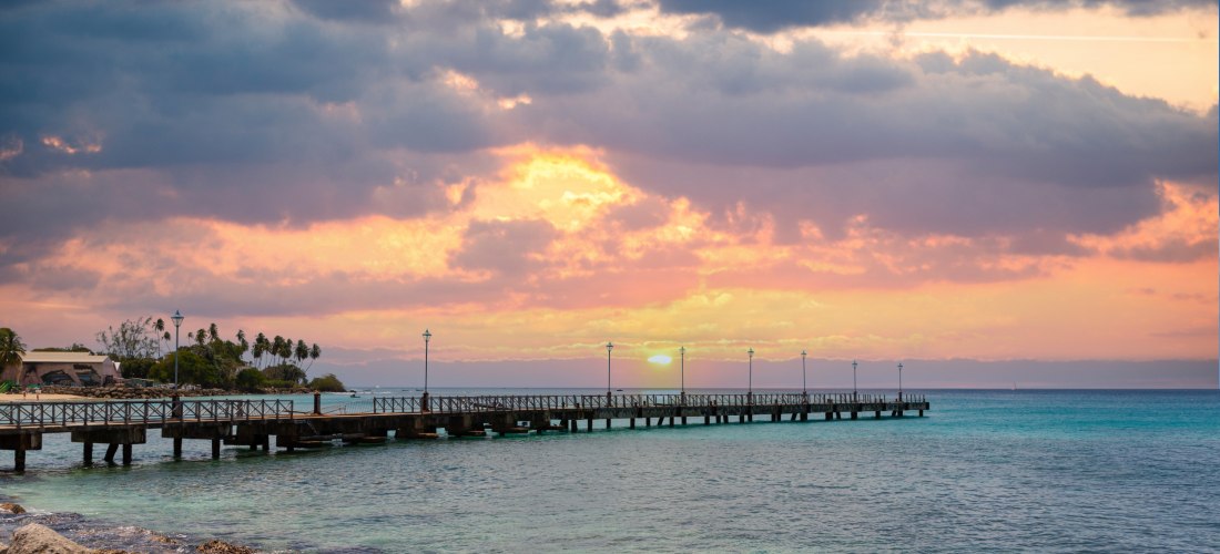 Sonnenuntergang über dem Meer auf Barbados mit Pier und orangefarbenem Himmel.