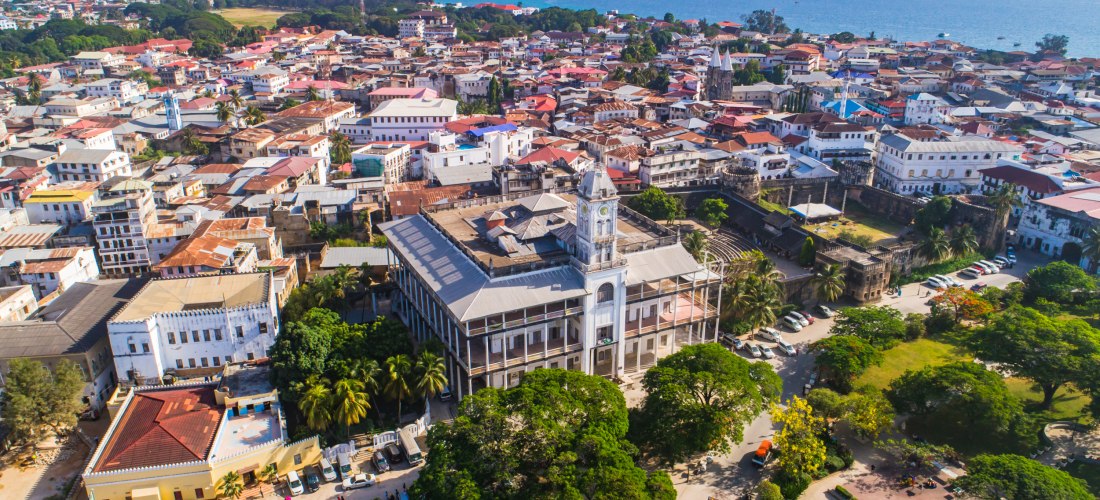 Stone Town auf Sansibar aus der Luft: House of Wonders mit Uhrturm, daneben das Old Fort, Dächer der Altstadt und Indischer Ozean im Hintergrund