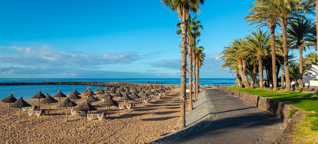 Strand von Playa de las Américas auf Teneriffa mit Palmenpromenade, Sonnenschirmen und goldenem Sand