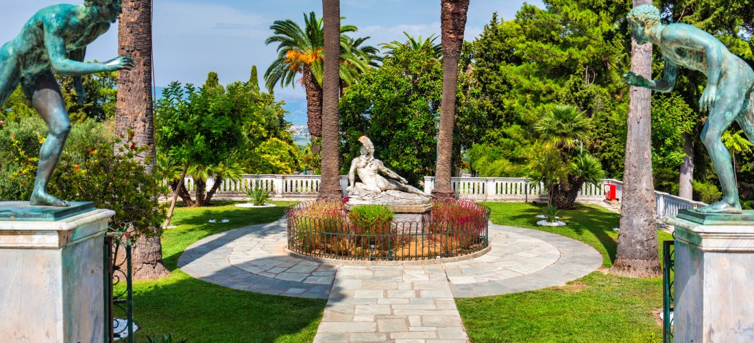 Statue des sterbenden Achill im Garten des Achilleion Palastes auf Korfu, umgeben von Palmen und Skulpturen