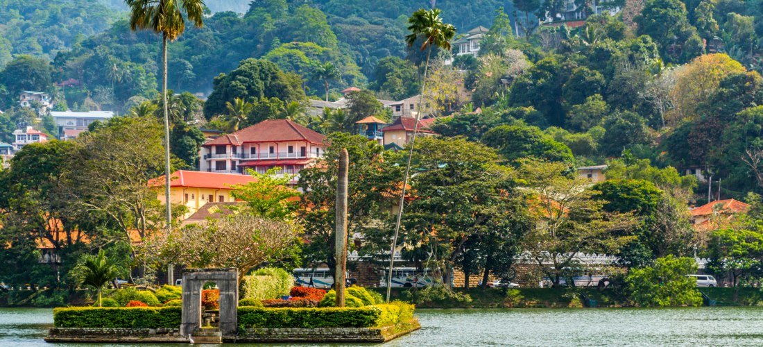 Kleine Insel mit Garten und Palmen im Kandy-See, umgeben von Hügeln und traditionellen Gebäuden in Sri Lanka