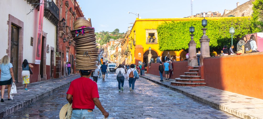 Straßenszene in San Miguel de Allende, Mexiko: Straßenverkäufer mit Hüten und bunten Häuserfassaden – Kolonialstadt 
