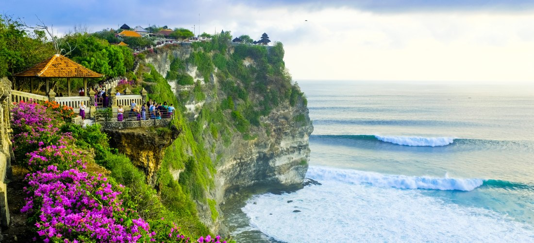 Aussichtsplattform am Uluwatu-Tempel auf Bali mit Besuchern, bunten Blumen und steilen Klippen über dem Meer