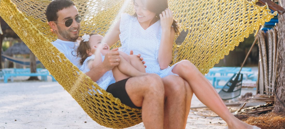Familie am Strand in Hängematte, 2 Erwachsene und 1 Kinde bei Sonnenschein