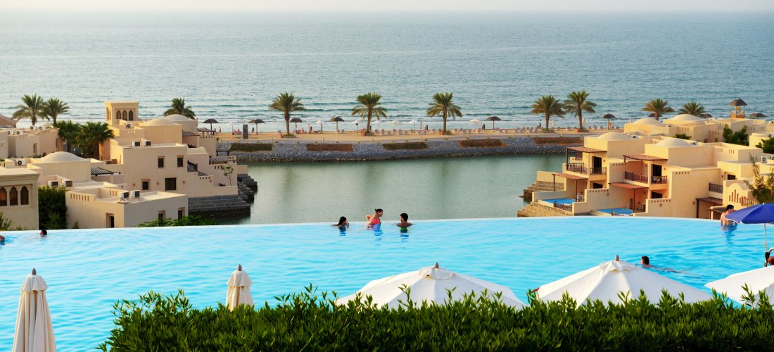 Infinity-Pool mit Blick auf ein luxuriöses Resort, Palmen, Sandstrand und das Meer im Hintergrund